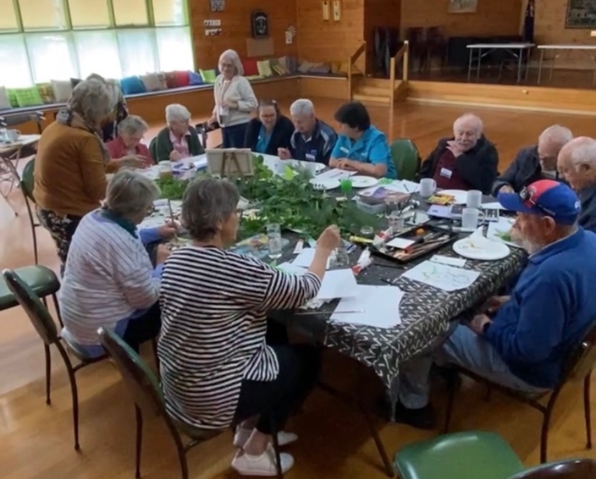 Members of the Art-Escape program around a long table, painting and drawing together